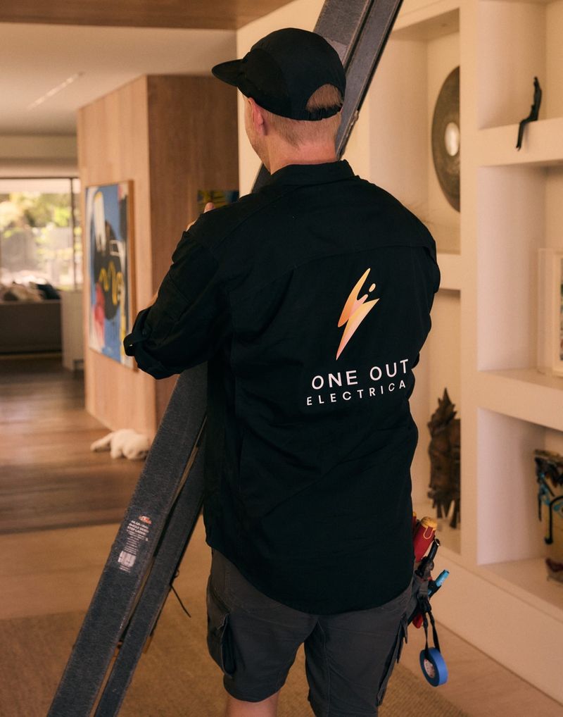 One Out Electrical electrician carrying a ladder through a high-end home interior — residential electrical services Hobart