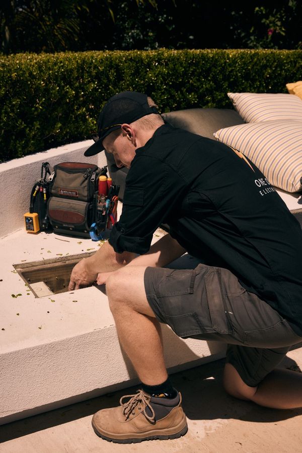 One Out Electrical electrician accessing an outdoor power junction box next to a garden wall