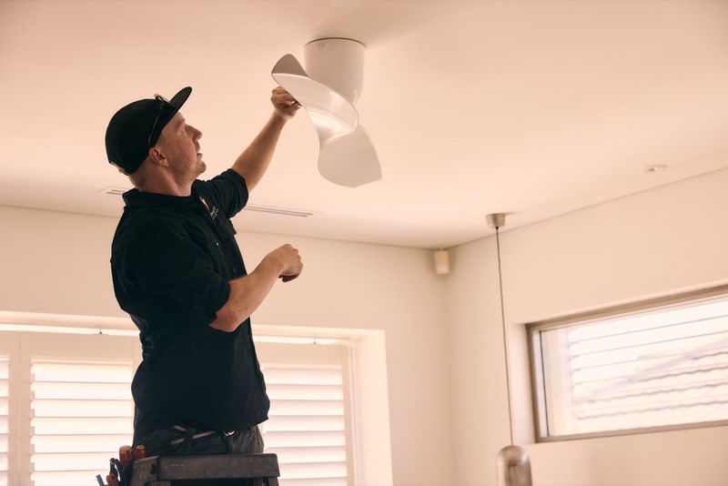 One Out Electrical electrician fitting ceiling fan blades during an installation in a bright bedroom