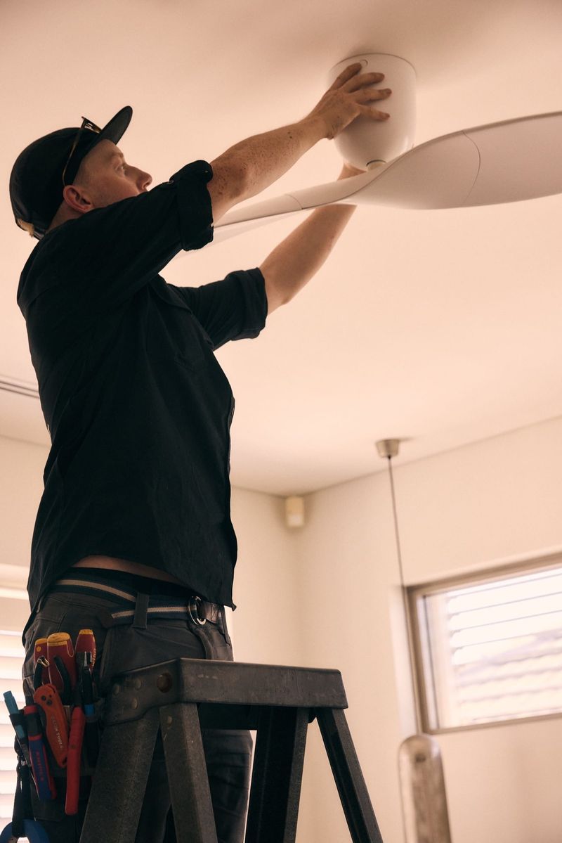 Electrician on a ladder attaching the canopy of a ceiling fan — residential fan installation Hobart