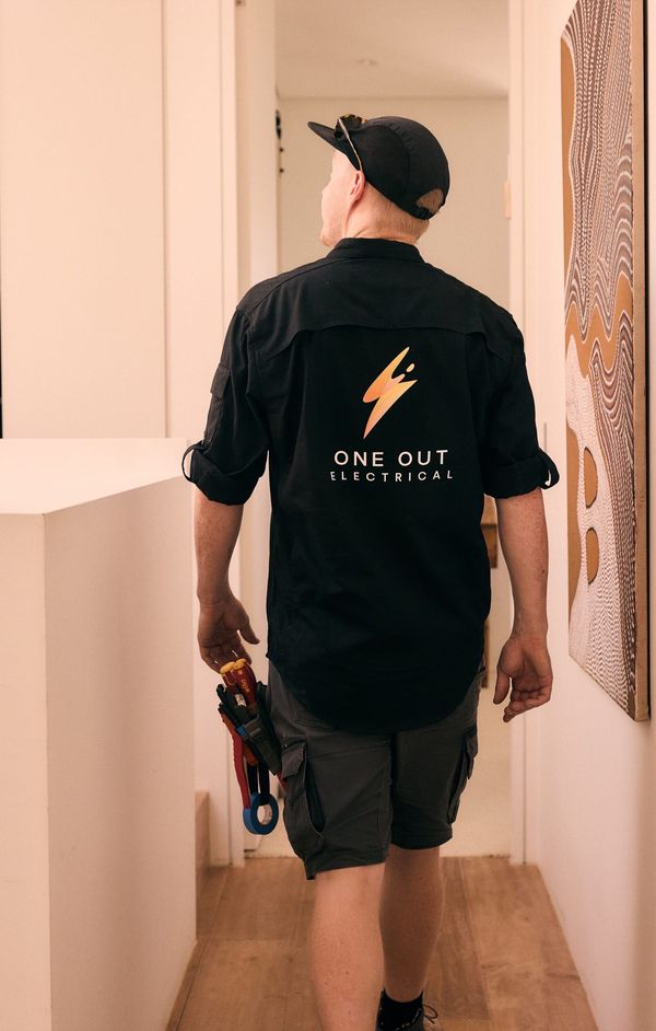One Out Electrical electrician walking through a hallway carrying pliers — ready for the next job