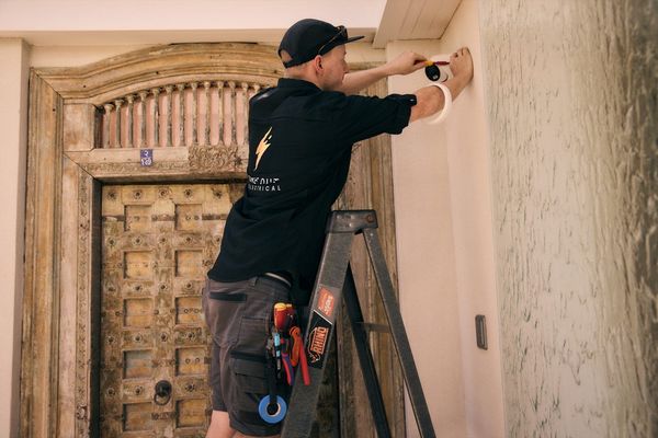 One Out Electrical electrician on a ladder installing a CCTV security camera above a front entrance