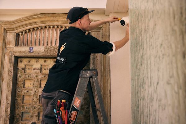 Electrician fitting a CCTV security camera above a doorway — security camera installation Hobart