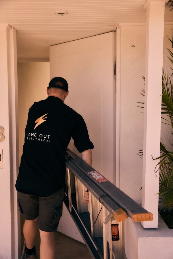 One Out Electrical electrician carrying a ladder into a residential property to begin a job