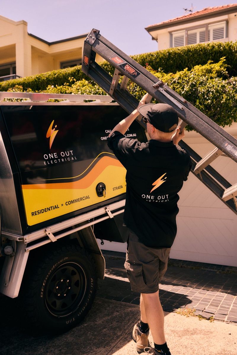 Electrician loading a ladder onto the One Out Electrical service vehicle roof rack before a job