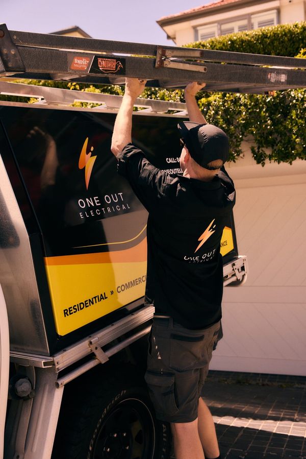 One Out Electrical electrician securing a ladder to the vehicle roof rack outside a Hobart home
