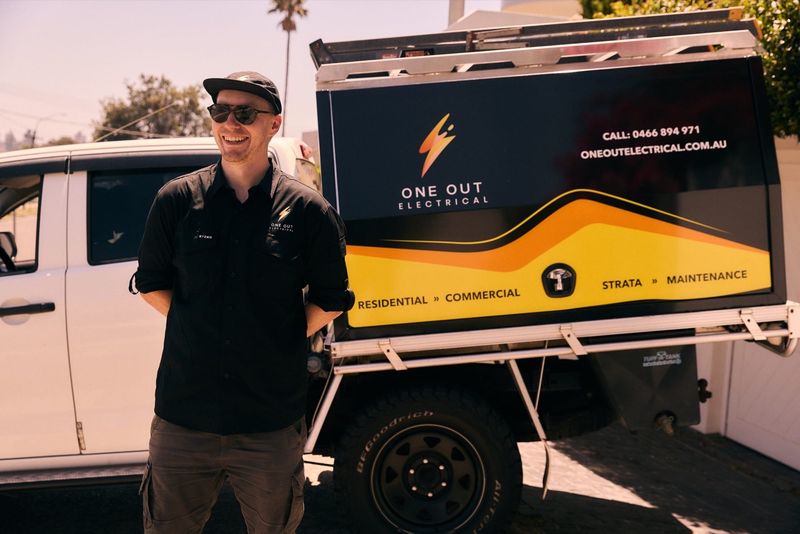 One Out Electrical electrician smiling beside the branded residential and commercial service ute in Hobart
